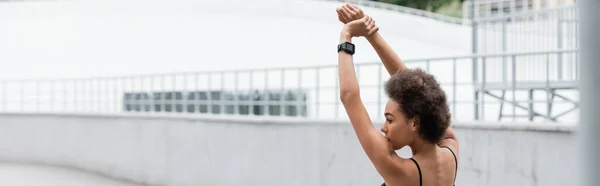 Side view of african american sportswoman with smart watch stretching on stadium, banner — Stock Photo