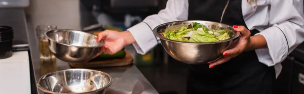 Cropped view of african american chef holding bowl with salad in professional kitchen, banner — стоковое фото