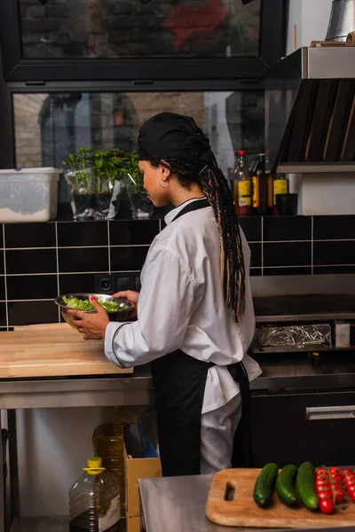 African american chef in apron holding bowl with lettuce — Stock Photo