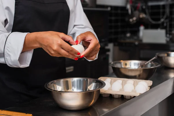 Partial view of african american chef holding raw egg above bowl while cooking in kitchen — Photo de stock