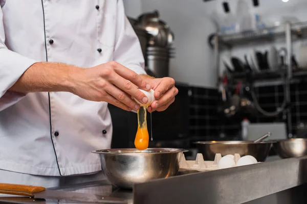 Cropped view of man breaking raw egg above bowl while cooking in kitchen - foto de stock