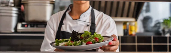 Cropped view of african american chef holding plate with freshly cooked salad in professional kitchen, banner - foto de stock