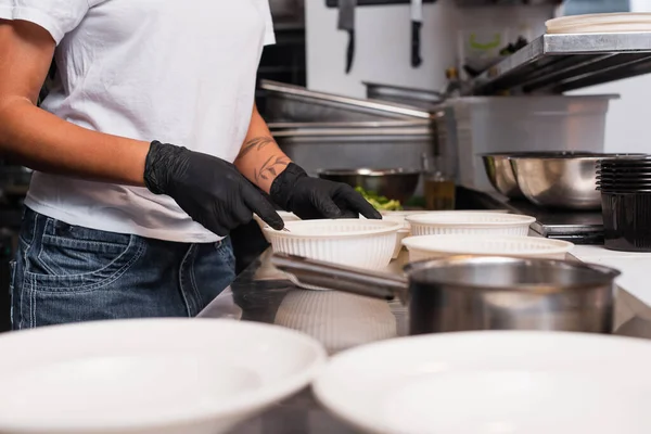 Partial view of tattooed african american woman holding plastic bowl with soup in kitchen — Photo de stock