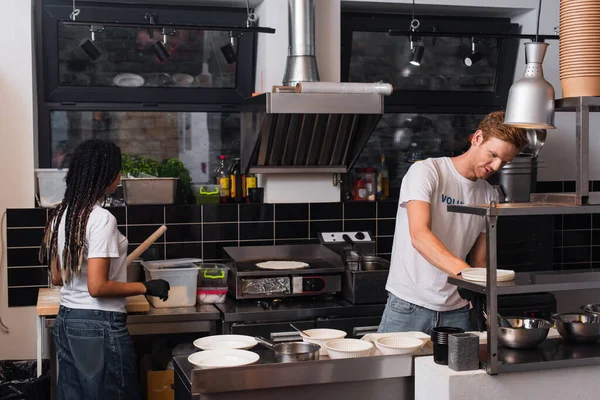 Young multiethnic volunteers in t-shirts cooking together in kitchen — Fotografia de Stock