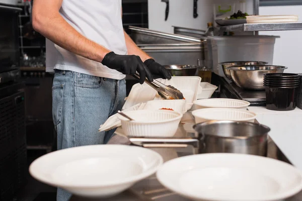 Cropped view of volunteer in latex gloves holding tweezers near plastic containers in kitchen - foto de stock