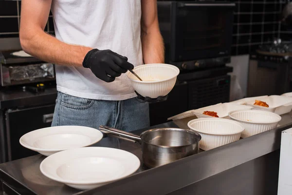 Обрізаний вид добровольця в латексних рукавичках, що тримає пластикову чашу на кухні — стокове фото
