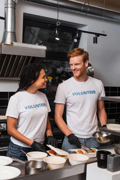 Happy multiethnic social workers in latex gloves putting prepared food into plastic containers — Foto stock