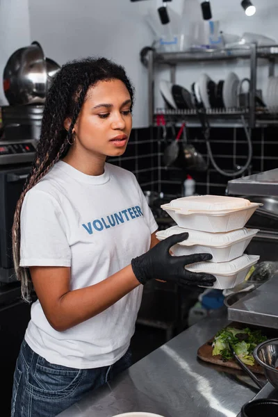 African american social worker holding plastic containers in kitchen — Stock Photo