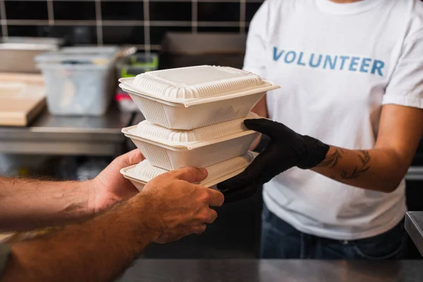 Cropped view of african american volunteer giving plastic containers with food to man — стоковое фото