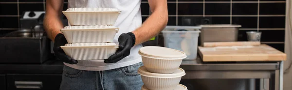 Cropped view of man in t-shirt with volunteer lettering holding plastic containers in kitchen, banner — стоковое фото