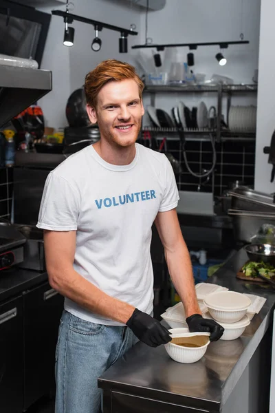 Happy redhead volunteer covering bowl with plastic cup in kitchen — Foto stock