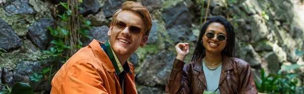 Happy multiethnic friends in sunglasses and jackets smiling in outdoor terrace, banner - foto de stock