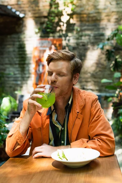 Redhead man drinking cocktail near prepared lunch in outdoor cafe terrace — Foto stock