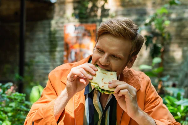 Cheerful and redhead man eating tasty quesadilla in crispy tortilla — Photo de stock