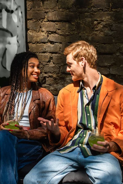 Cheerful multiethnic friends holding glasses with cocktail while talking outside - foto de stock