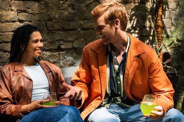 Happy multiethnic friends holding glasses with cocktail while talking outside — Fotografia de Stock