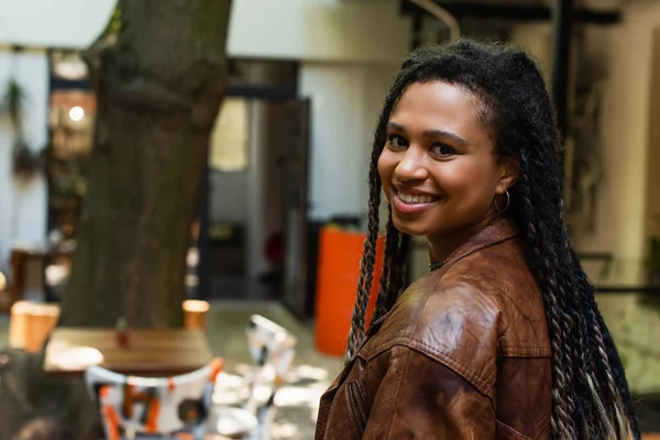 Joyful african american woman in brown leather jacket smiling outside — Foto stock