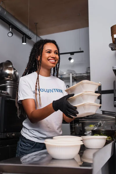 Smiling african american social worker holding plastic containers in kitchen — Fotografia de Stock