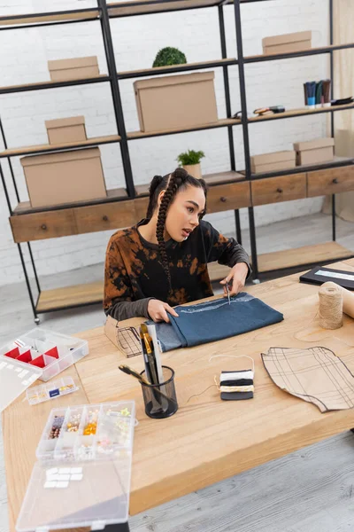 African american designer talking on smartphone near cloth and sewing equipment in worktop — Stockfoto