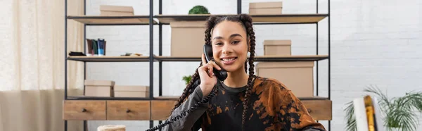 Smiling african american designer talking on telephone in workshop, banner - foto de stock