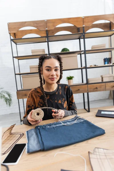 Young african american craftswoman holding twine near cloth and smartphone in workshop — Foto stock