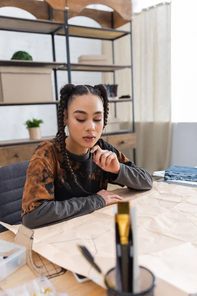 African american craftswoman looking at sewing pattern near blurred cloth — Stock Photo