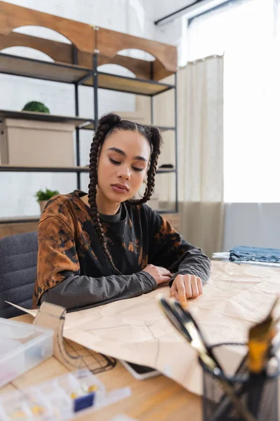 African american designer looking at sewing pattern near blurred equipment in workshop — Foto stock