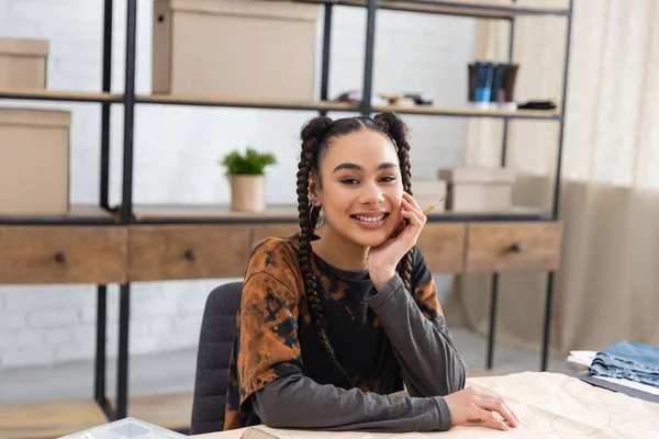 Smiling african american designer looking at camera near sewing pattern in workshop — Photo de stock