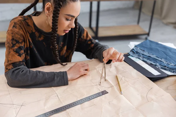 African american designer drawing with compass on sewing pattern in workshop — Foto stock