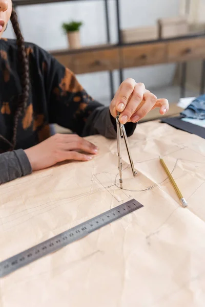 Cropped view of african american designer drawing with compass on sewing pattern near pencil — Photo de stock