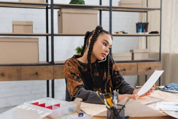 African american designer talking on smartphone and holding sketch in workshop — Foto stock