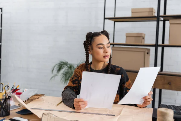 Young african american designer holding papers near sewing patterns in workshop — Stock Photo