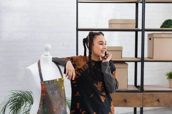 Smiling african american craftswoman talking on smartphone near apron on mannequin in workshop — Photo de stock