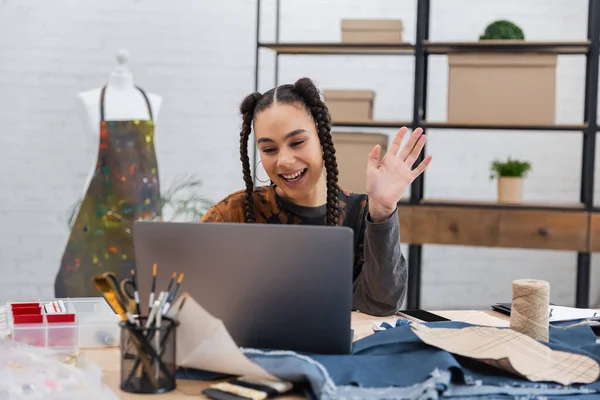 African american designer having video call on laptop near blurred sewing equipment in workshop — Foto stock