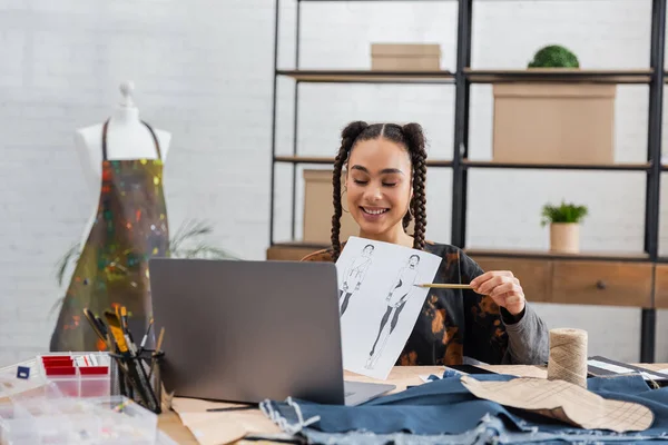 African american designer pointing at sketch during video call on laptop - foto de stock