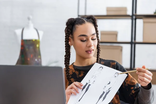 African american craftswoman pointing at sketch during video call on laptop - foto de stock
