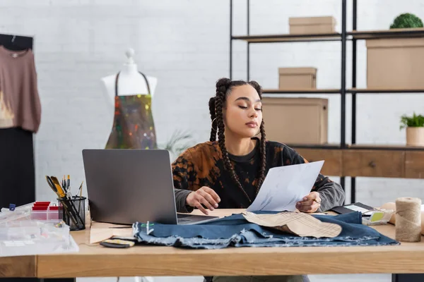 African american designer holding sketch near laptop and sewing equipment — Photo de stock