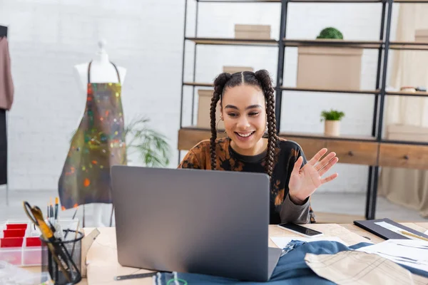 Smiling african american craftswoman having video call on laptop near smartphone and sewing equipment — Stock Photo