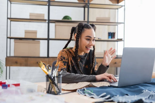 Smiling african american craftswoman having video call on laptop near sewing pattern and cloth on table — Stock Photo