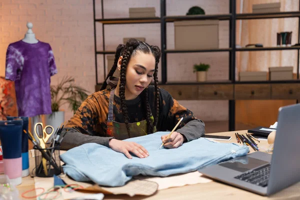 African american designer drawing on cloth near devices in workshop — Stock Photo