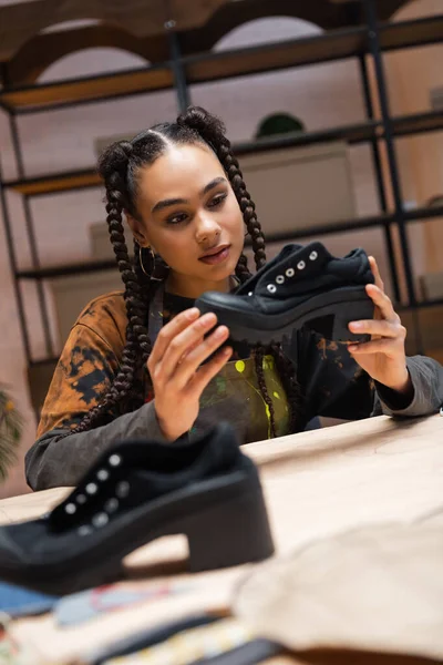 Африканська американська ремісниця тримає взуття біля розмитого візерунка шиття в майстерні. — стокове фото