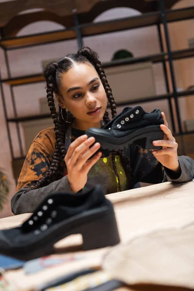 African american craftswoman holding shoe near blurred sewing pattern in workshop — Stock Photo