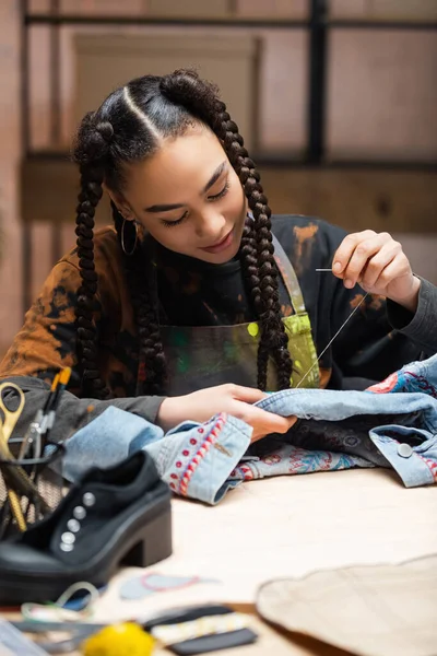 Young african american craftswoman embroidering denim jacket in workshop — Photo de stock