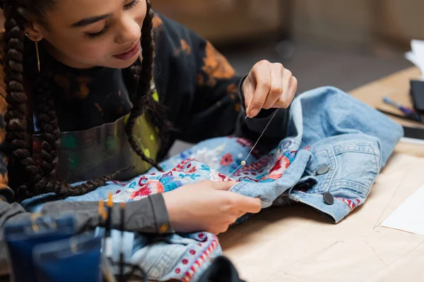 African american designer decorating denim jacket with embroidery in workshop — Foto stock