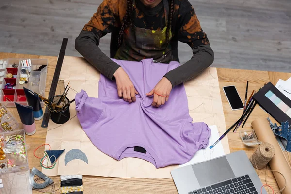 Cropped view of african american craftswoman working with t-shirt in workshop — Stock Photo