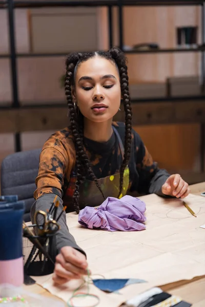 Young african american designer taking sewing equipment near cloth in workshop — Stock Photo