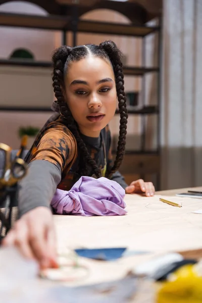 African american craftswoman taking blurred sewing equipment near cloth in workshop — Stock Photo