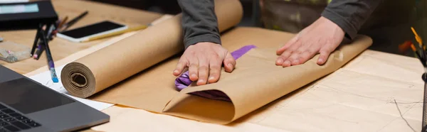 Cropped view of african american designer packaging clothes near laptop and smartphone in workshop, banner — Stock Photo