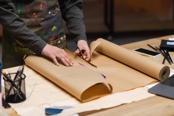 Cropped view of african american craftswoman cutting craft paper while packaging clothes in workshop — Stock Photo