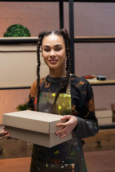 Smiling african american designer holding carton box in workshop — Stock Photo